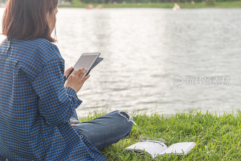 一个女人坐在湖边，在平板电脑屏幕上敲击