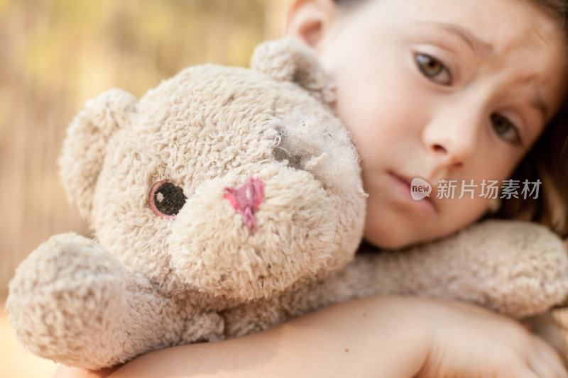 悲伤的小女孩拥抱着外面破旧的泰迪熊