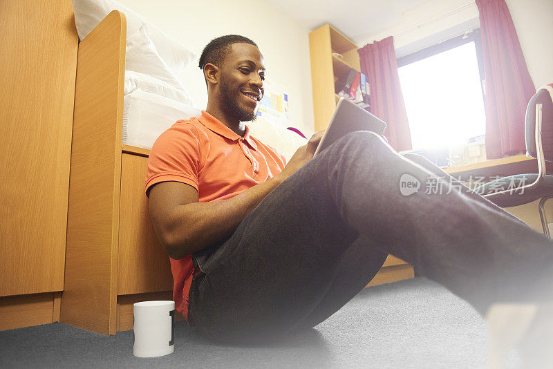 一名大学生坐在宿舍地板上使用平板电脑
