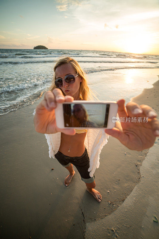 一个年轻女子在日落时在海滩上拍照