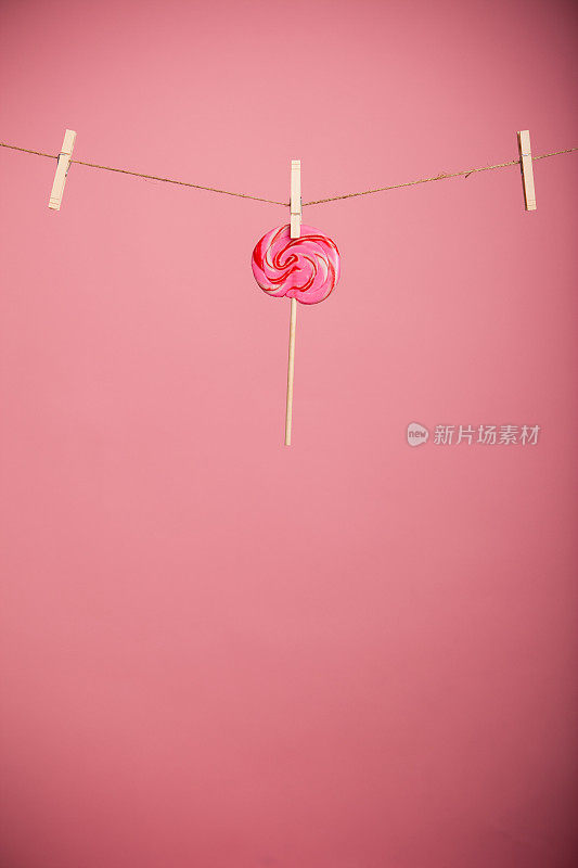在粉红色背景下，挂在晾衣夹上的旋涡棒棒糖