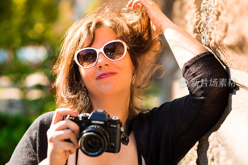 年轻快乐的女摄影师拿着数码相机，在户外玩头发