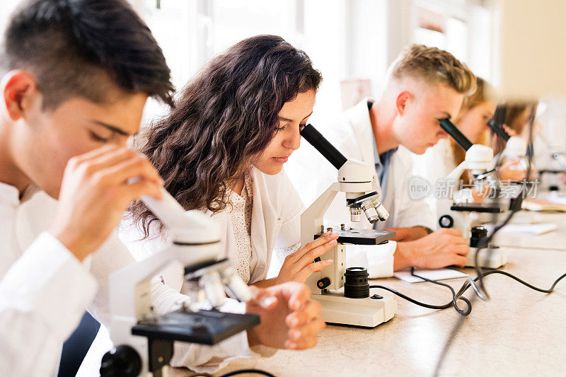 漂亮的高中生在实验室里拿着显微镜。
