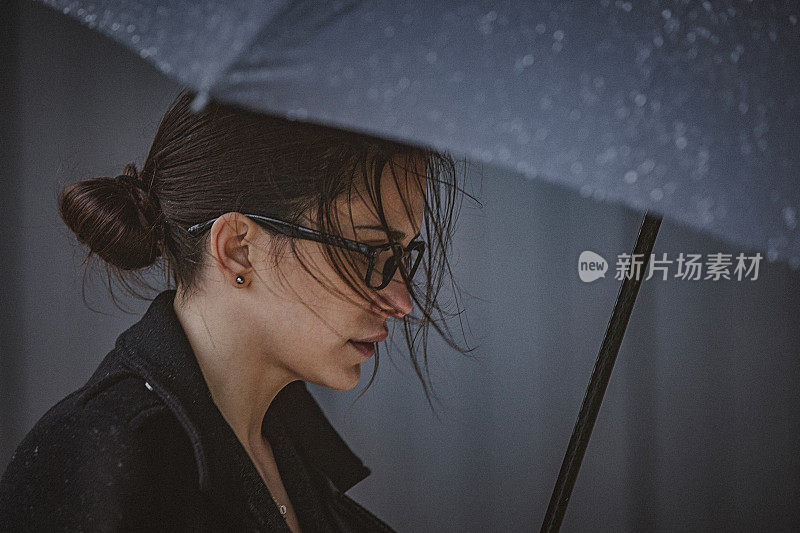 一名年轻女子撑着伞，在寒冷的秋日里在风雨中行走。