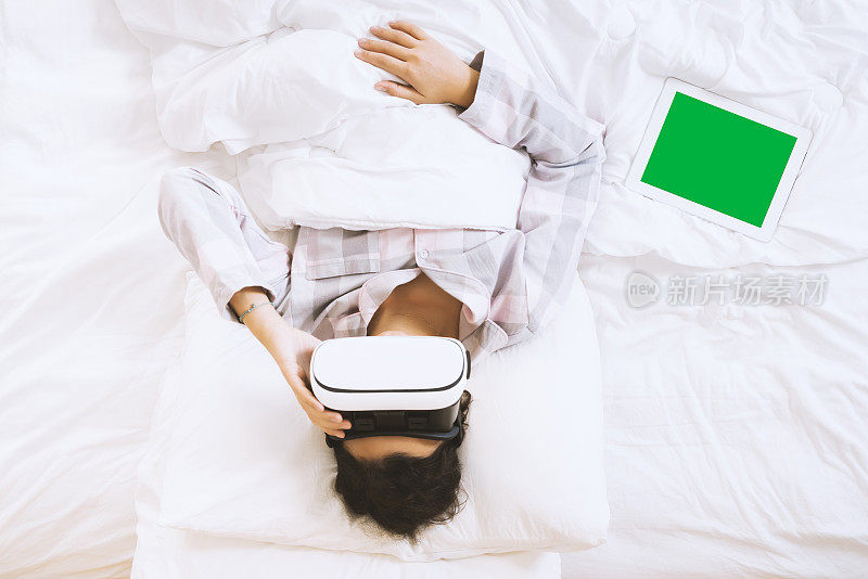 女人戴着VR眼镜，躺在床上用着绿屏平板电脑