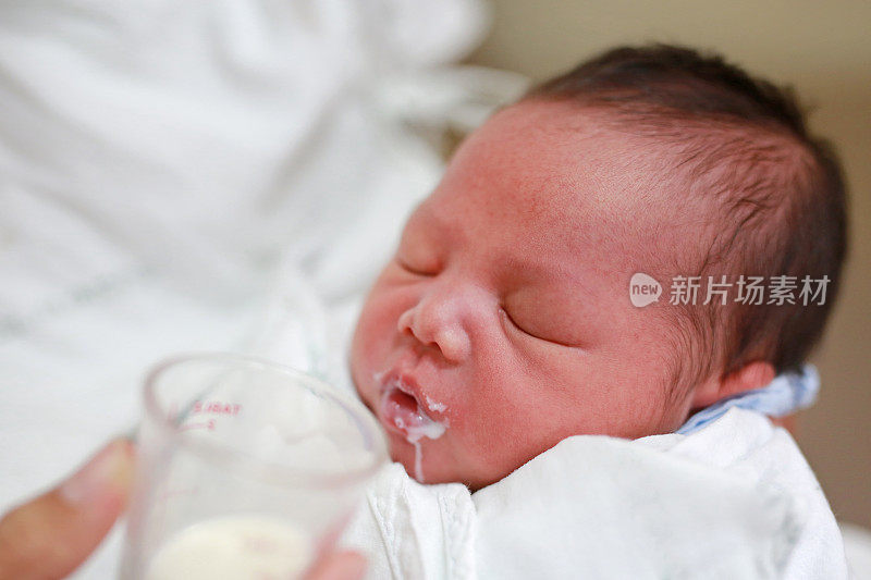 母亲用玻璃杯给婴儿喂奶。