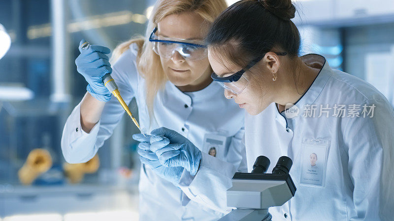 医学研究科学家把样品滴在载玻片上，她的同事在显微镜下检查它。他们在一个现代化的实验室工作。