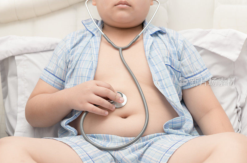 胖男孩用听诊器检查胃。