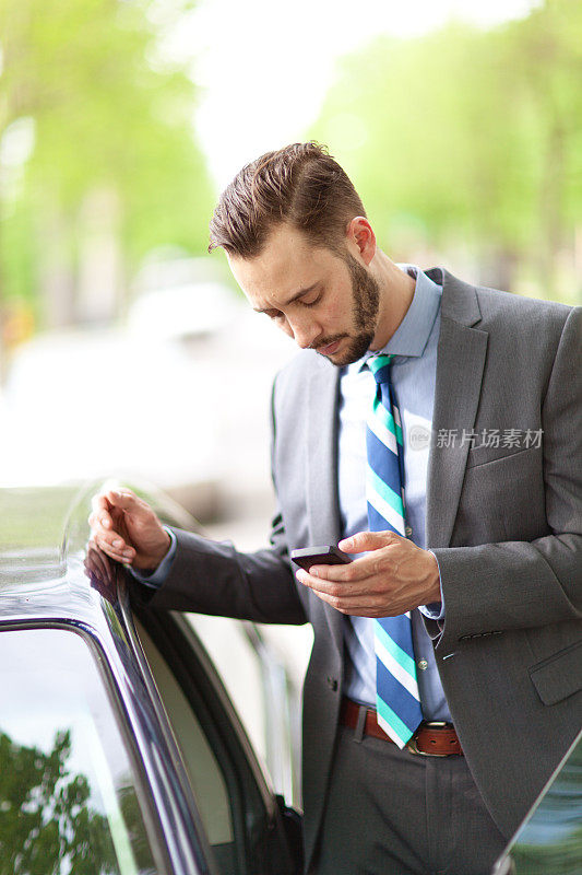 白人年轻商人站在他的车旁用手机打电话