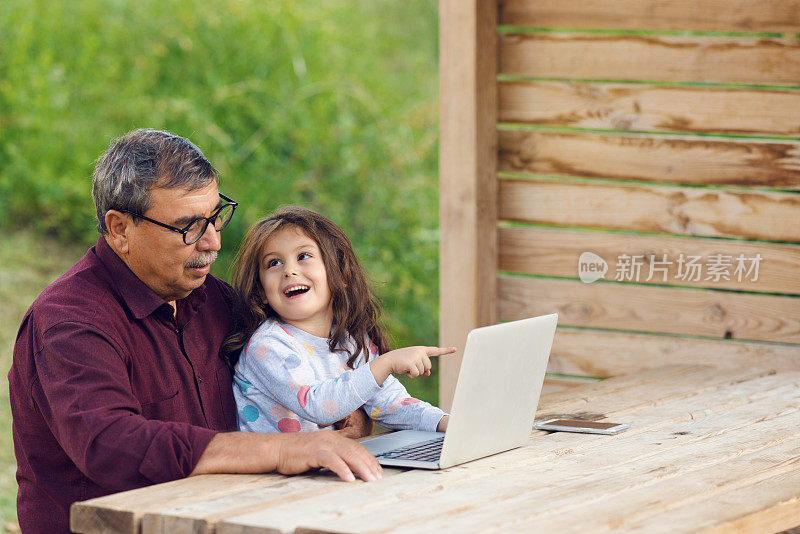 小女孩和爷爷一起用笔记本电脑