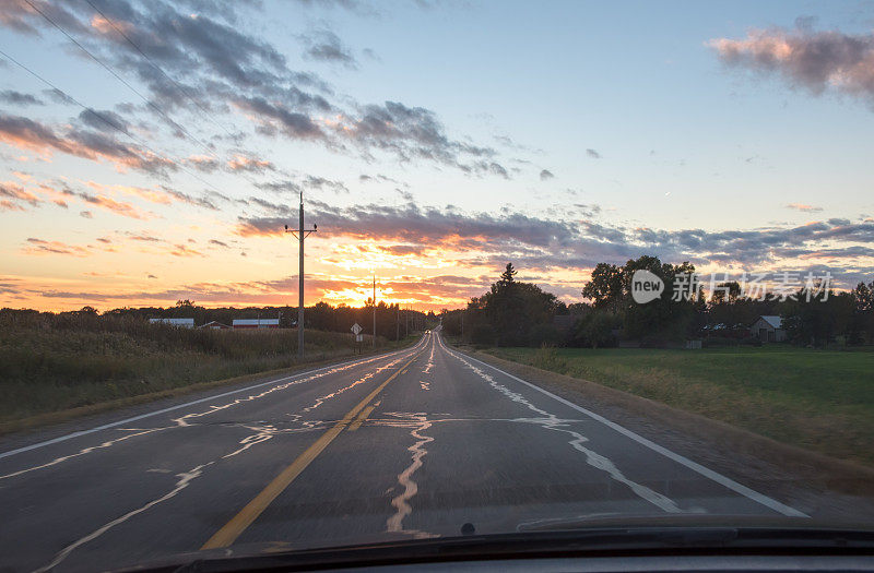 在乡村道路上开车的时候，夕阳在戏剧性的天空中低垂