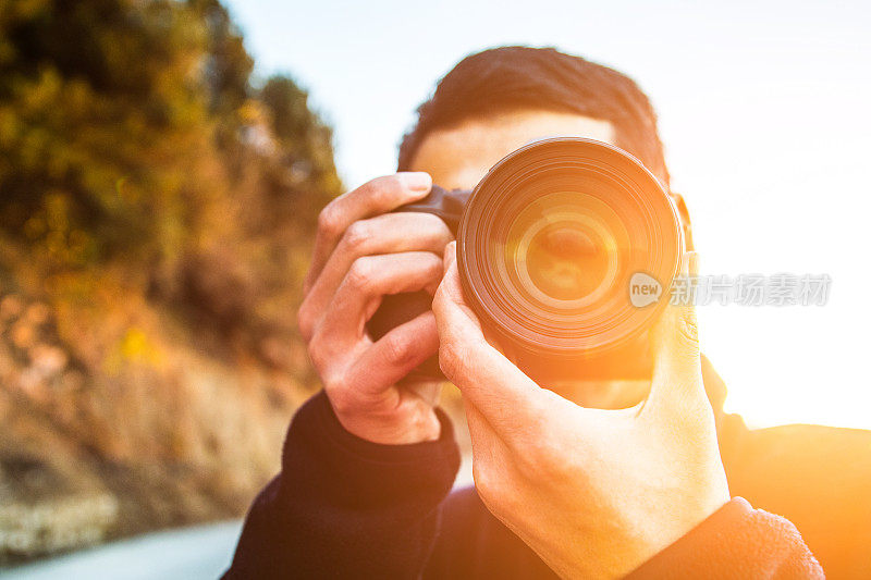 年轻男子在日落时用相机拍照的特写