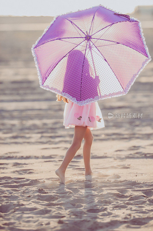 年轻美丽的女孩走在海滩上带着伞