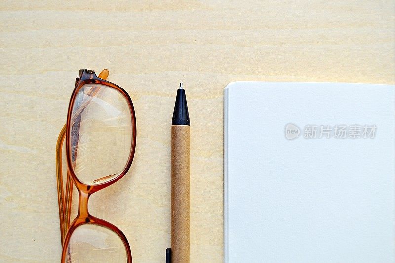 一副眼镜的水平照片，一支钢笔和一张白色的笔记本，放在一个木制的米色水平背景上，很有美感。