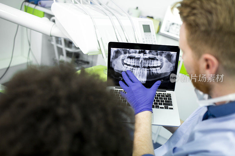 牙医在笔记本电脑上向病人展示全景牙科x光图像