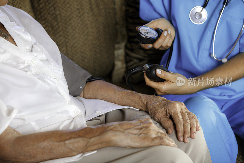 养老院的援助。年轻的西班牙女医生给老年妇女测血压