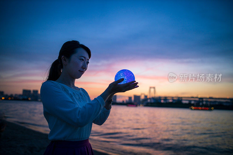 年轻女子在日落海滩拿着彩球