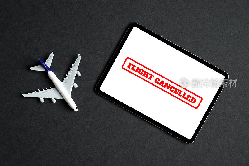 航班取消的概念。黑色背景屏幕上显示“航班取消”字样的飞机型号和平板电脑。平躺，俯视图。
