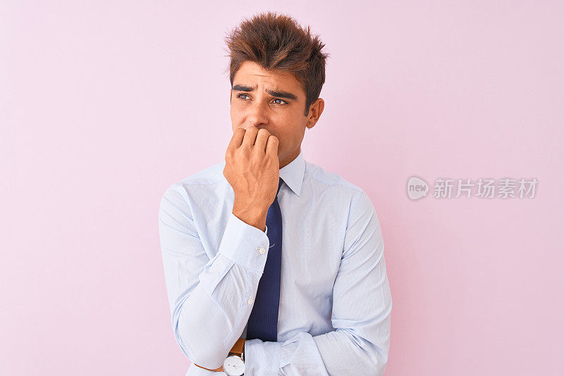 年轻英俊的商人穿着衬衫和领带站在孤立的粉红色背景看起来紧张和紧张的手在嘴咬指甲。焦虑的问题。