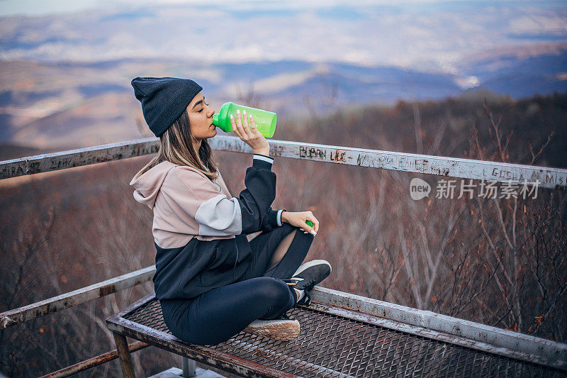 美丽的女孩坐在长椅上，喝着水