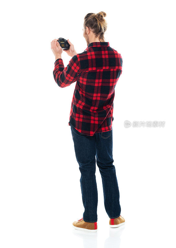白人男性摄影师穿着裤子拿着相机站在白色背景前