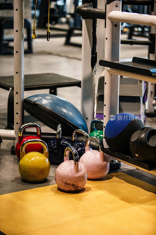 壶铃和实心球躺在健身房其他健身器材旁边的地板上