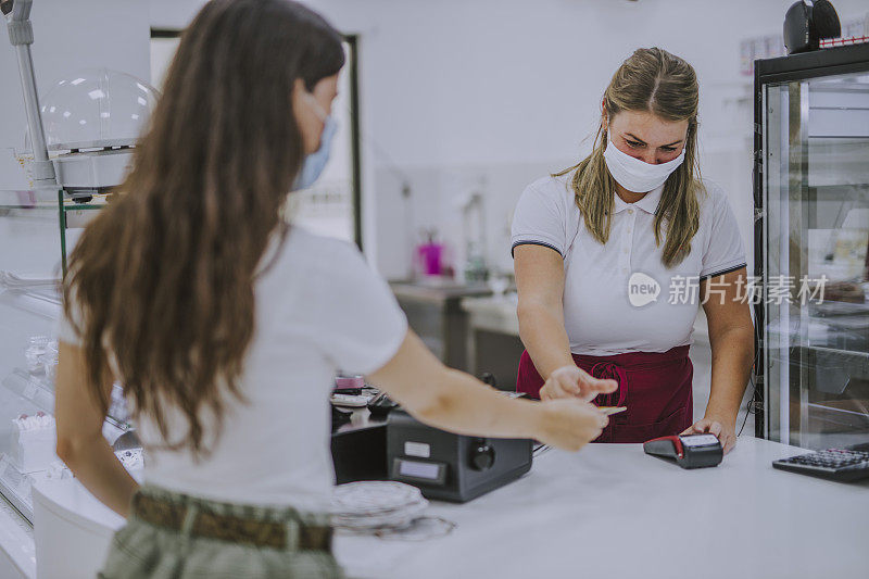 现代女性在蛋糕店支付非接触者的费用，并佩戴防护口罩，以预防冠状病毒和其他疾病