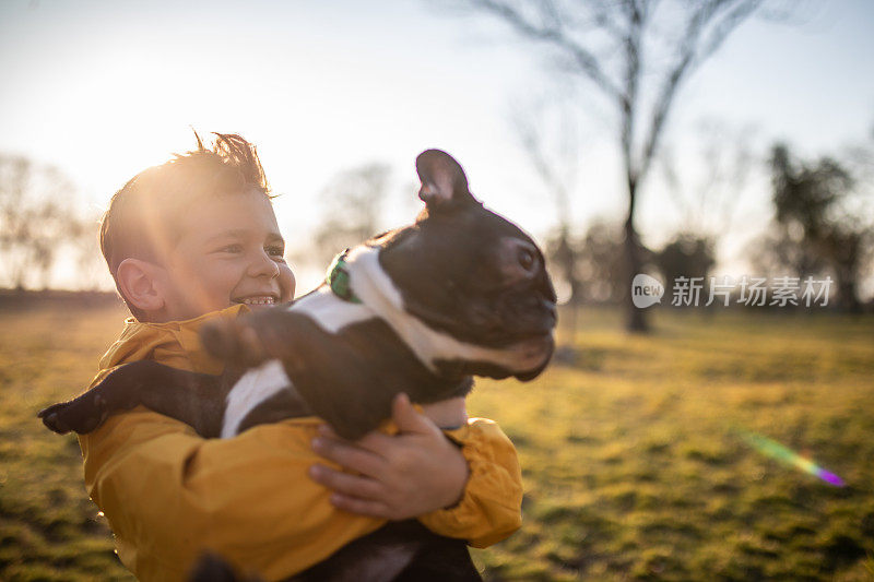一个可爱的男孩抱着一只法国斗牛犬在公园里