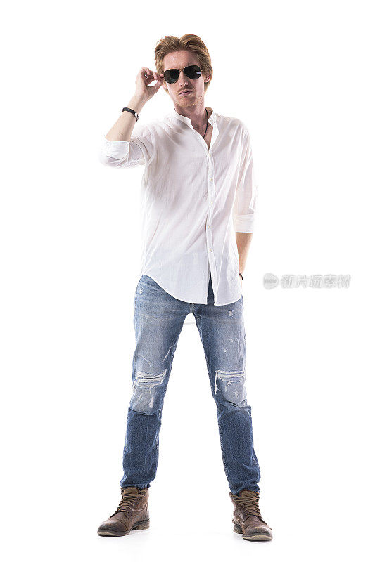 骄傲的年轻时尚男模特在牛仔裤和白色衬衫拿着太阳镜