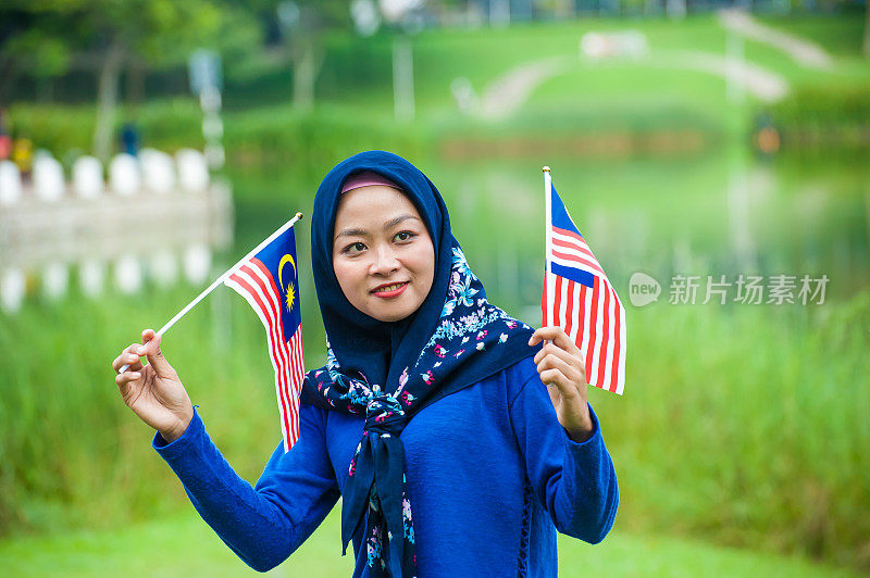 年轻的马来西亚妇女戴着头巾，挥舞着马来西亚国旗，以高度的爱国主义精神在公园庆祝独立日