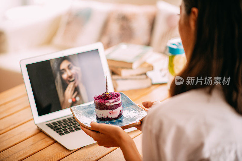 一位女士一边用笔记本电脑聊天，一边用生日蛋糕庆祝朋友的生日