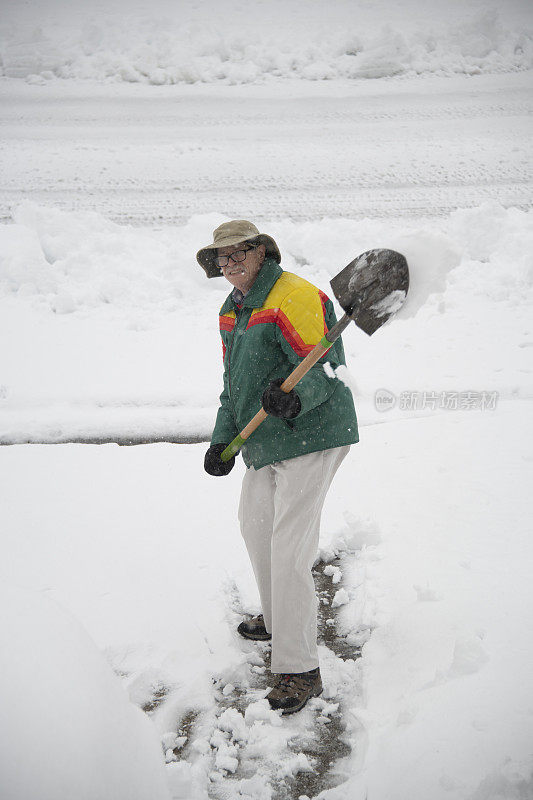 穿绿夹克的老人正在铲雪