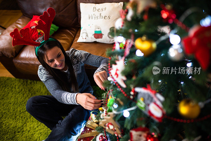 一个漂亮的年轻女人坐在圣诞树下，挂着装饰品