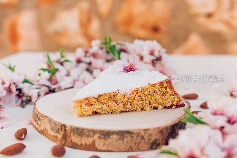 来自马略卡岛的美味杏仁蛋糕Gató放在木片上，上面装饰着杏仁花、花瓣和新鲜的碎杏仁