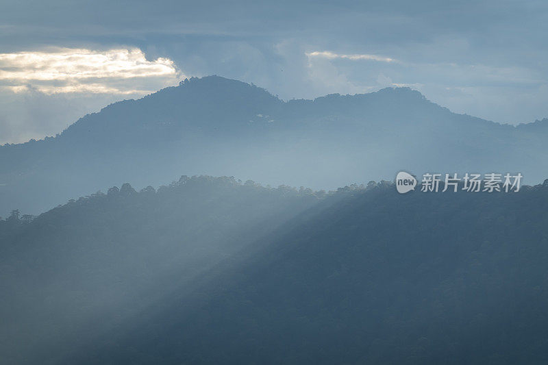 太阳光线透过云层在山谷的山丘上被穿透云层的太阳光线照亮