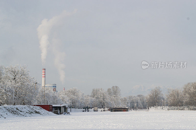 从工业烟囱里冒出来的烟，烟幕映衬着雪景，远处的群山，在一个下雪天