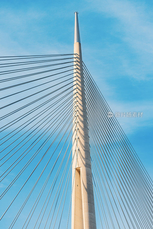 作为现代工程奇迹，这座悬索桥横跨河流，背景是湛蓝的天空，展示了复杂的钢索建筑