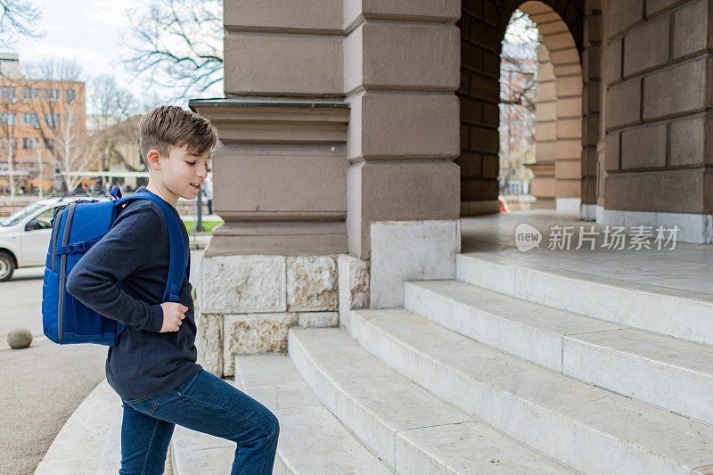 第一天上学，一个男生背着书包站在学校大楼附近的楼梯上。回到学校。教育。