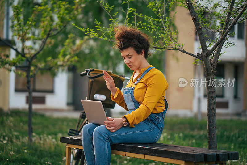 一名女子在进行在线视频通话时向坐在长凳上的笔记本电脑挥手