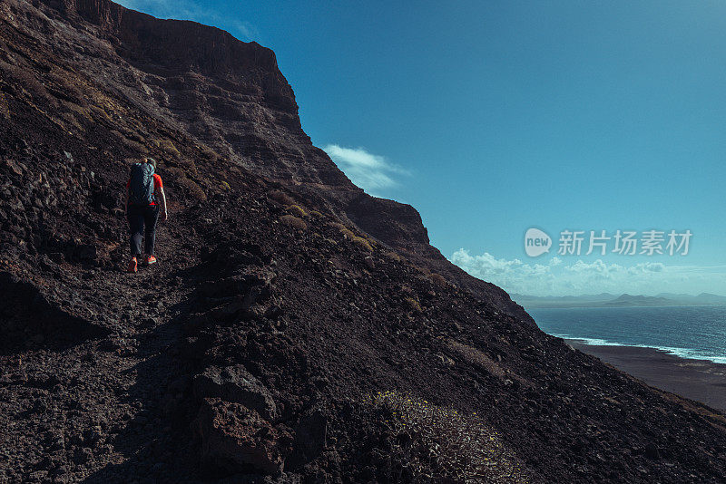 在加那利群岛兰萨罗特岛的火山海岸风景中徒步旅行的妇女