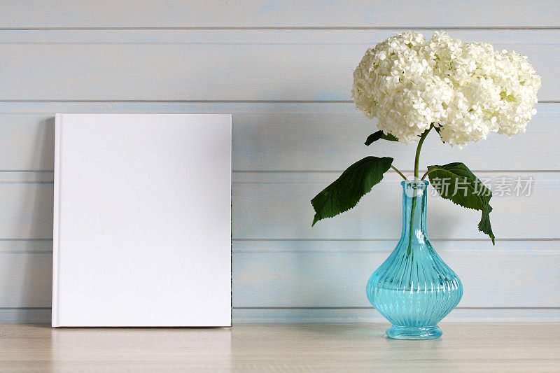 书或画册的模型小册子的空封面。桌上的蓝色花瓶里插着一枝盛开的绣球花。背景，复制空间。为你的设计留出空间。