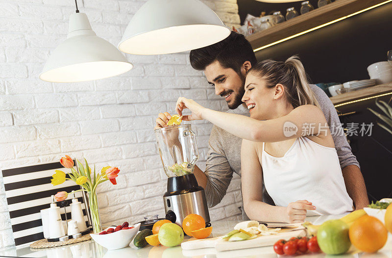 一对年轻夫妇在食品加工机里搅拌水果，做奶昔
