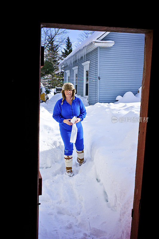 成熟的女人在冬天的雪地里走向户外厕所。