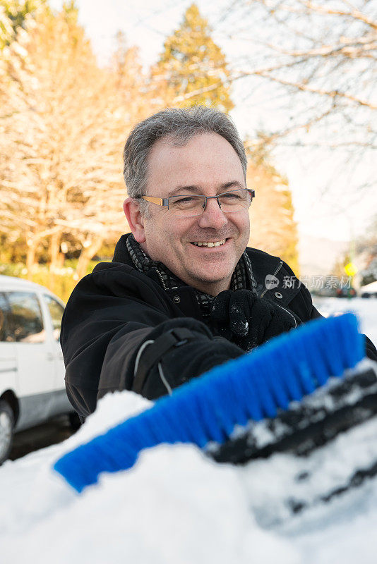 在居民区，一个成熟的男人正在清理车窗上的雪