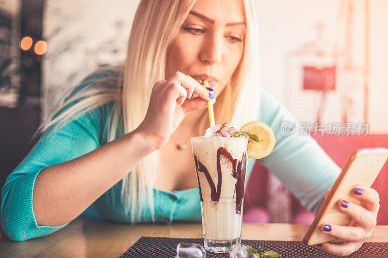 一个拿着智能手机和一杯冰沙坐在桌子旁的女人