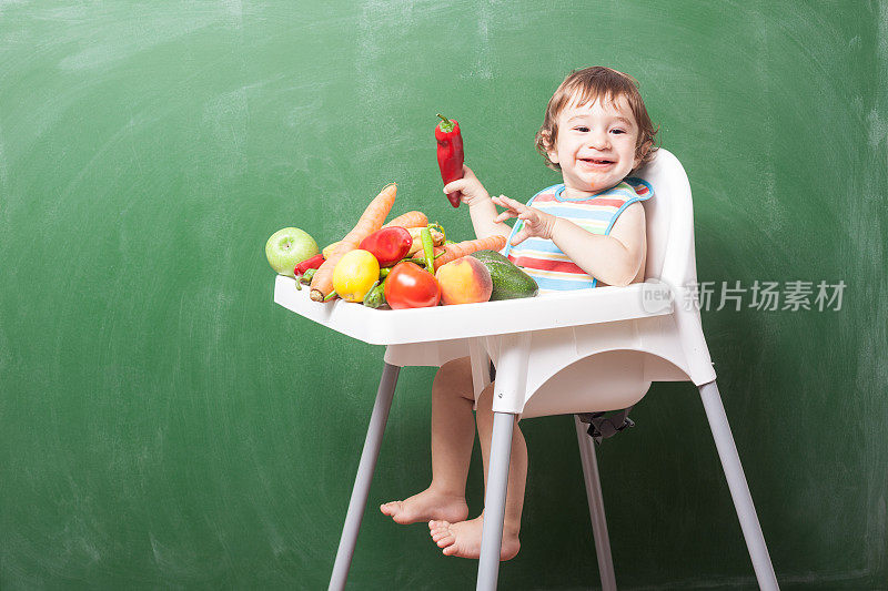 小男孩在绿色黑板前的高椅子上吃东西