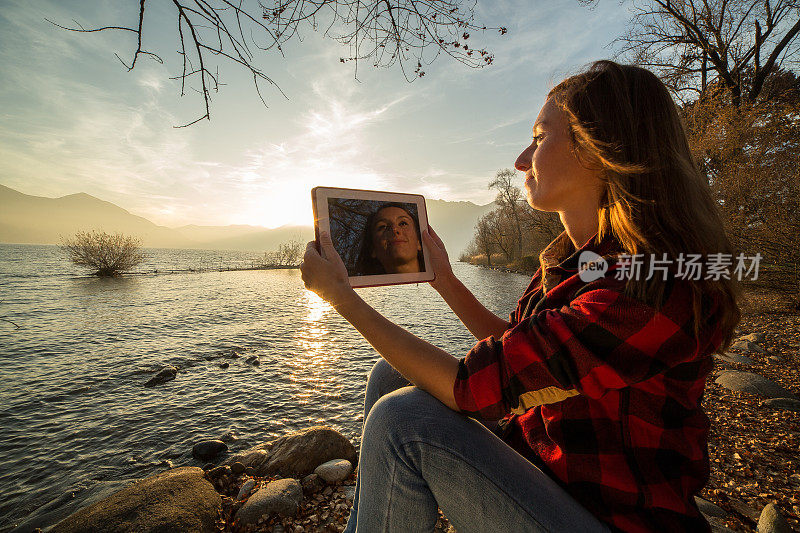 年轻女子坐在湖边，用着平板电脑