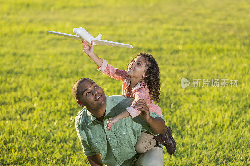 西班牙女孩骑在父亲的背上玩玩具飞机