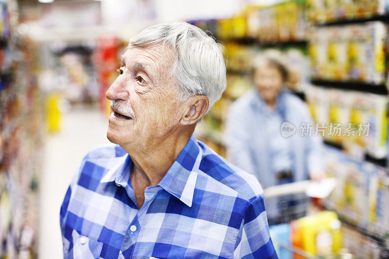 一位严肃的高级男子在超市货架上寻找东西