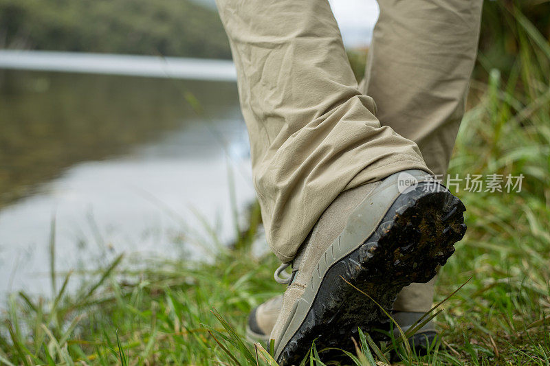 人的腿和徒步靴站在一个山湖边